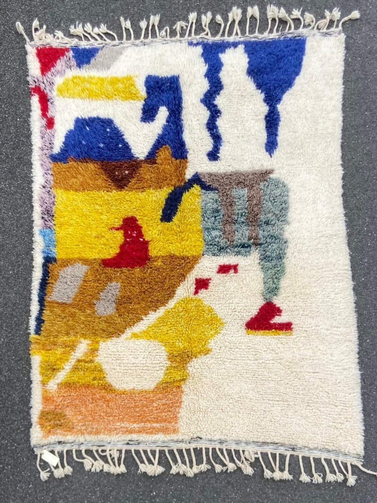 Front view of a handwoven multicolor rug with an abstract pattern and fringe edges on a gray background.