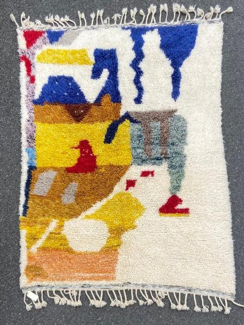 Front view of a handwoven multicolor rug with an abstract pattern and fringe edges on a gray background.