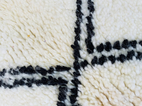 Close-up of a white Moroccan rug featuring a geometric black pattern and textured surface.