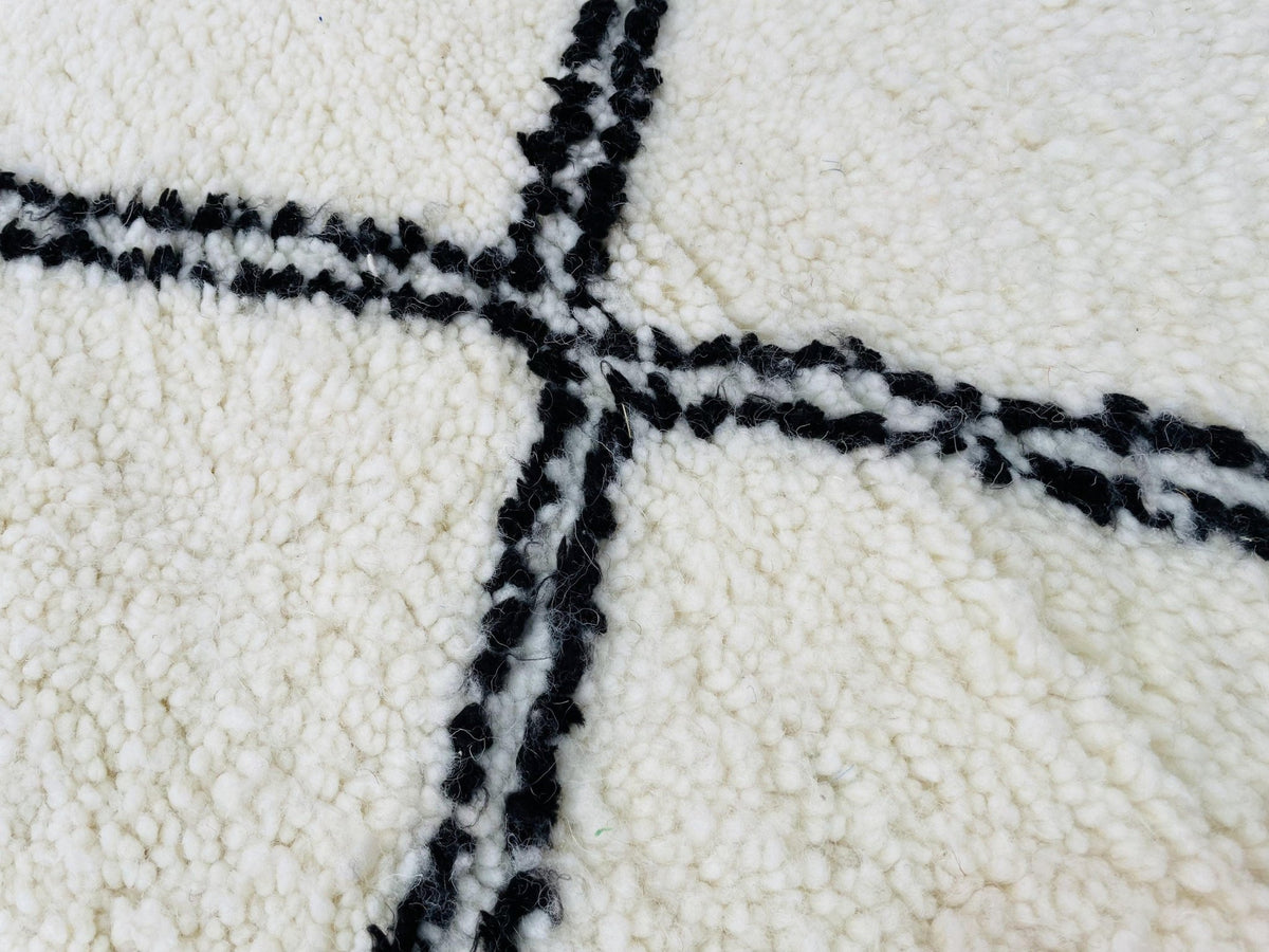 Close-up view of a white rug with a black geometric pattern and textured surface.