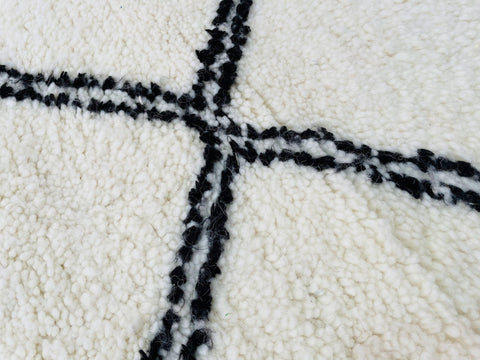 Close-up view of a white rug with a black geometric pattern and textured surface.