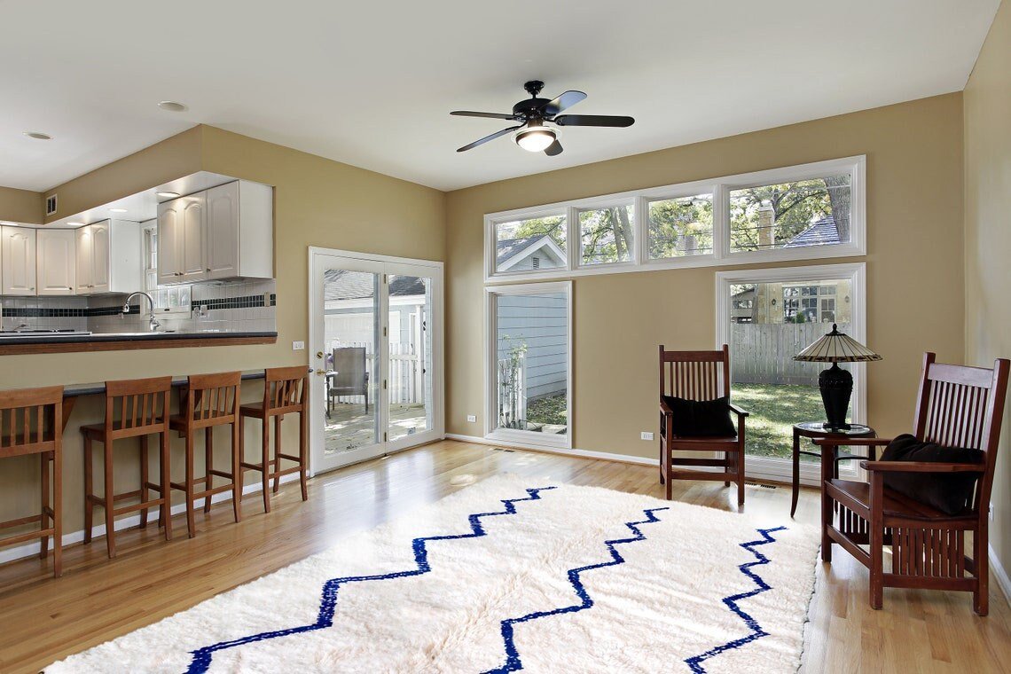 Lifestyle shot of a blue striped Beni Ourain Moroccan rug in a living room with wooden furniture and large windows.