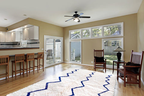 Lifestyle shot of a blue striped Beni Ourain Moroccan rug in a living room with wooden furniture and large windows.