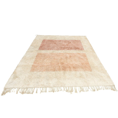 Lifestyle shot of a beige and pink geometric abstract rug with fringed edges in a natural setting