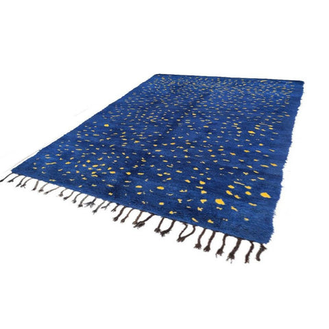 Side view of a blue Moroccan rug showcasing fringe edges against a solid color background.