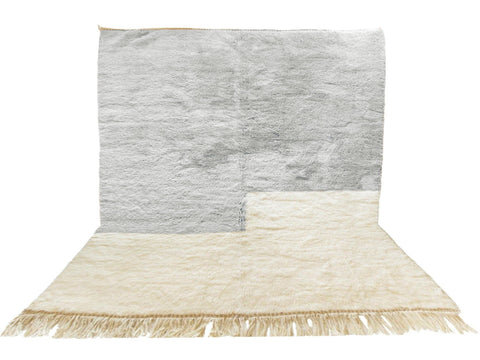 Lifestyle shot of a gray and white Moroccan rug with fringe edges on a natural background.
