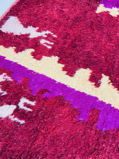Close-up detail of the abstract Moroccan rug with red, purple, and beige colors.