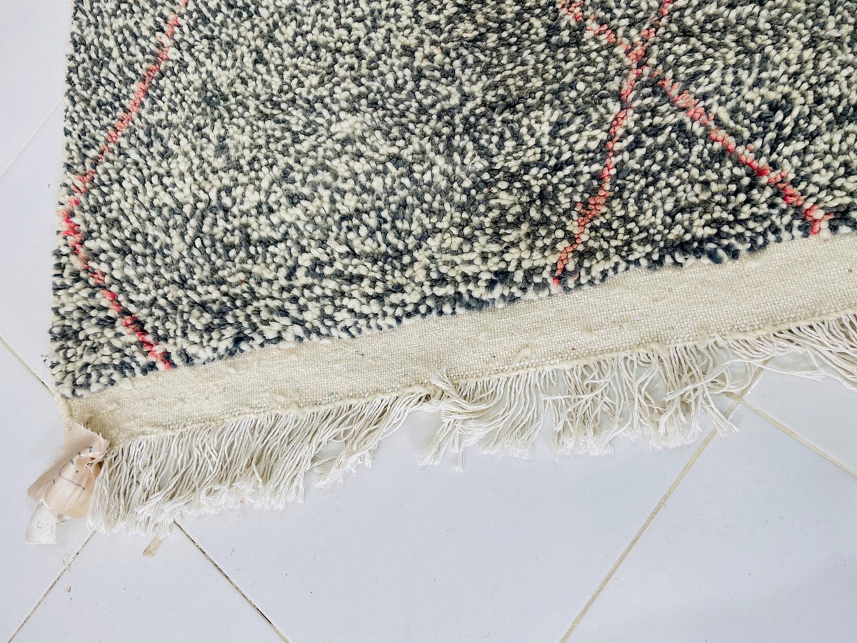Close-up detail of the edge of a gray geometric Beni Ourain Moroccan rug highlighting the woven pattern and fringe.