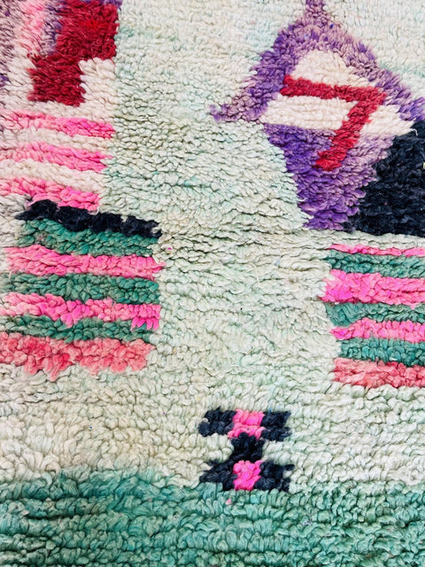 Detail shot of an abstract Moroccan rug featuring geometric patterns in blue, red, green, and pink.
