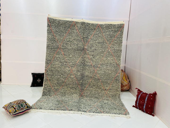 Lifestyle shot of a gray geometric Beni Ourain Moroccan rug with blue and red accents on a white background.