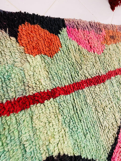 Close-up detail of a colorful Moroccan rug featuring abstract designs in green, red, orange, and pink.