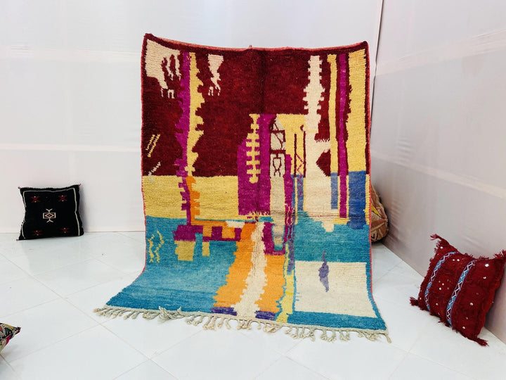 Lifestyle shot of the abstract Moroccan rug featuring blue, red, and yellow colors on a white background.
