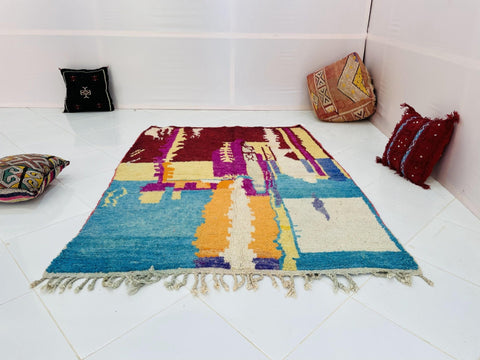 Top view of the abstract Moroccan rug showcasing blue and red colors with fringe edges.