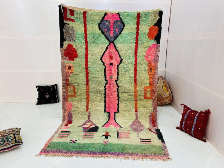 Lifestyle shot of a colorful Moroccan rug featuring abstract designs in green, pink, black, and red.