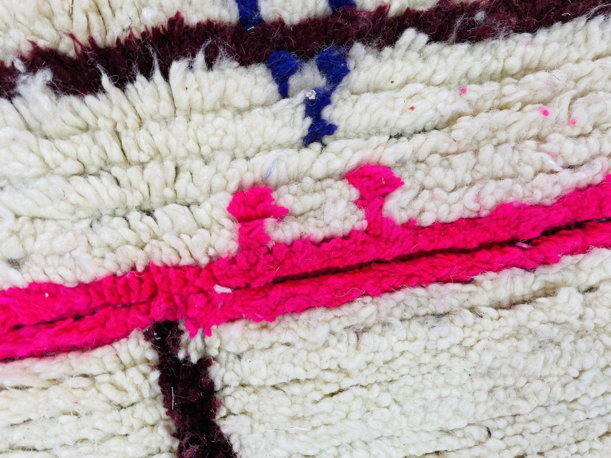 Close-up of a handmade Moroccan rug with a geometric design in white and pink.