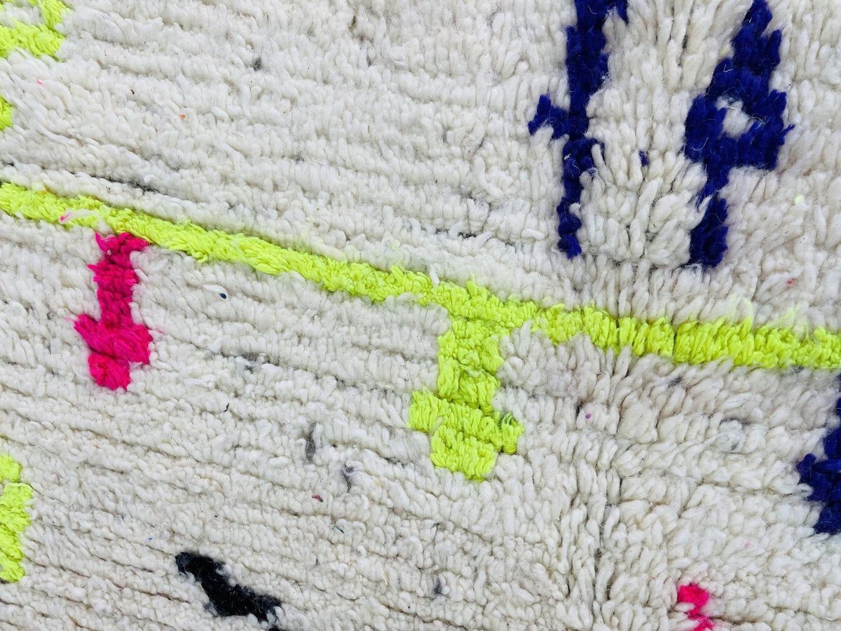 Detail view of a handmade Moroccan rug displaying white, neon green, and pink textured patterns.