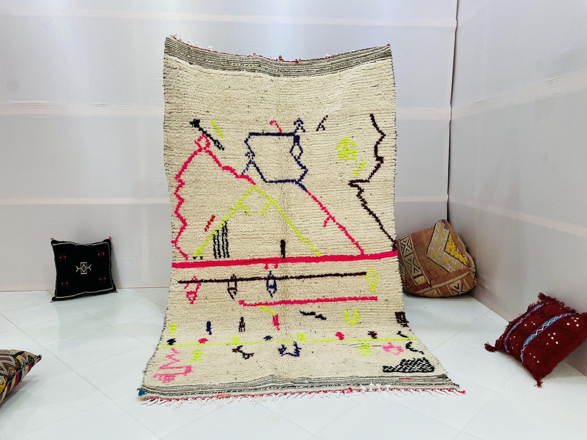 Lifestyle shot of a cream and red Moroccan rug with geometric patterns in a studio setting.