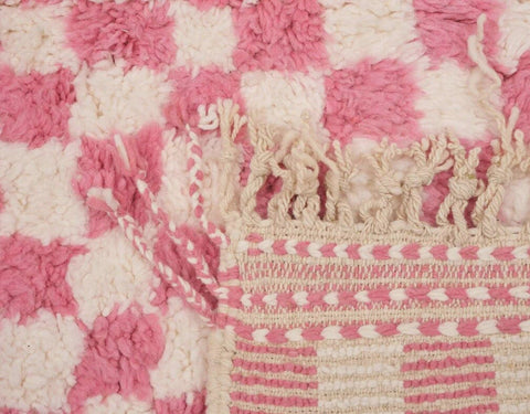 Side view of the pink checkered Beni Ourain rug with visible fringe edges.