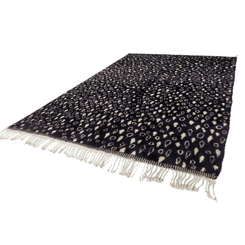Detail close-up of a plush black and beige abstract rug with a leopard pattern.