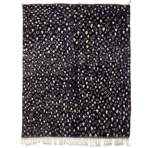 Detail close-up of a textured black and beige abstract rug with fringe edges.