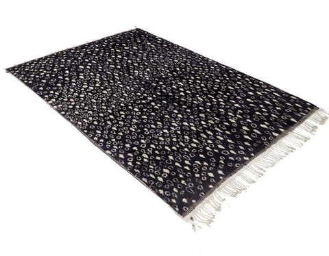 Side view of a textured black and beige abstract rug with fringe edges.