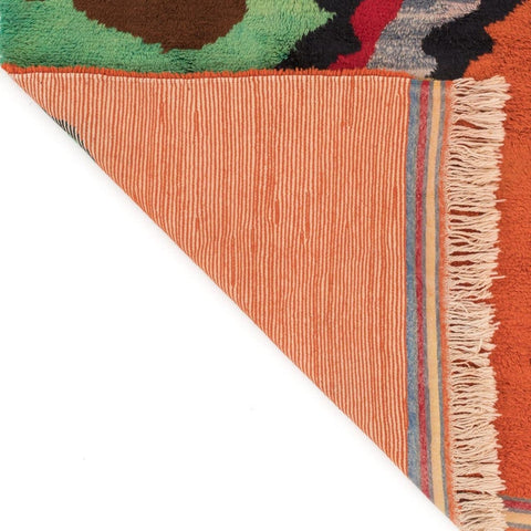 Close-up detail of the corner of the orange rug showcasing textured surface and fringe.