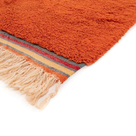 Detail shot of the edge of the orange rug displaying a striped pattern and fringe.