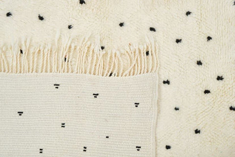 Close-up detail of an off-white rug showing a black polka dot pattern and fringe.