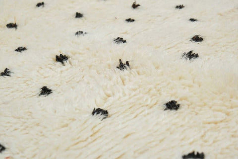 Close-up detail of an off-white rug featuring a black polka dot pattern and fringe.