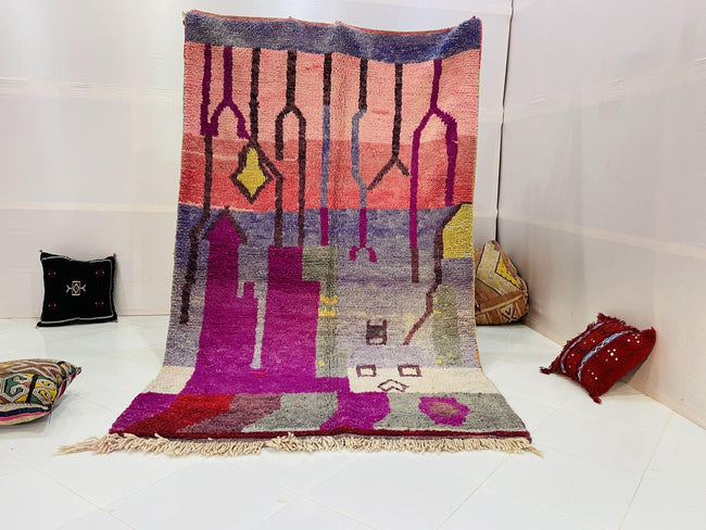 Lifestyle shot of a vintage Moroccan rug featuring purple and pink geometric patterns on a white background.