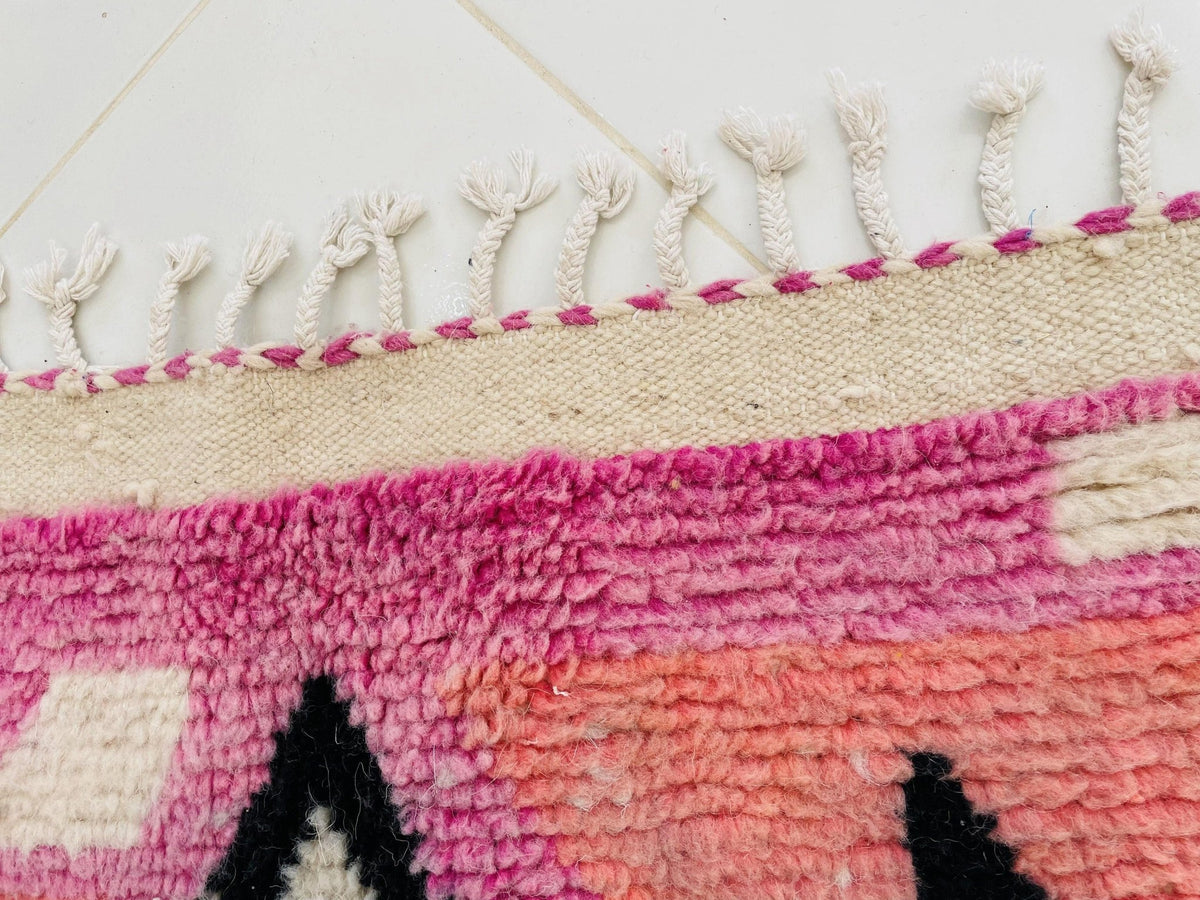 Detail close-up of the fringe edge of a purple and pink patterned Moroccan rug.