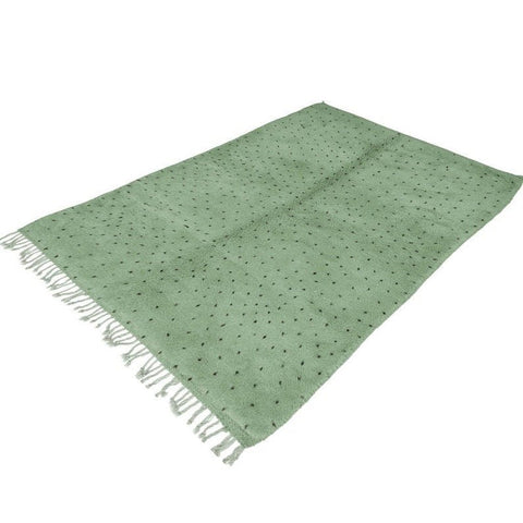 Side view of sage green rug with white dots and fringe edges.