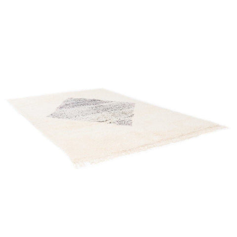 Detail view of the cream rug with a diamond pattern and fringed edges.
