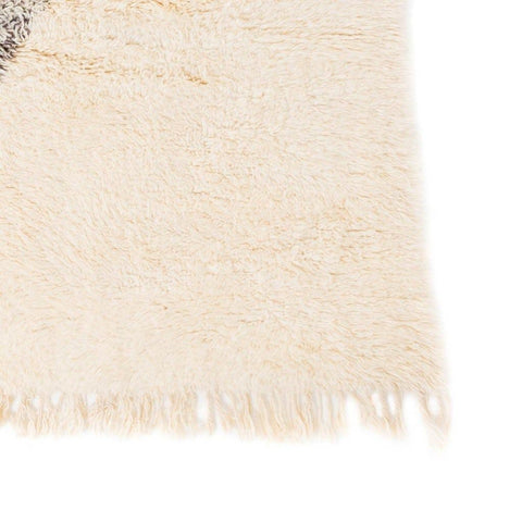 Detail close-up of the cream rug featuring fringed edges on a white background.