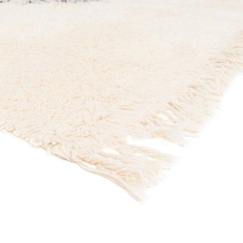 Detail close-up of the cream rug with fringed edges against a white background.