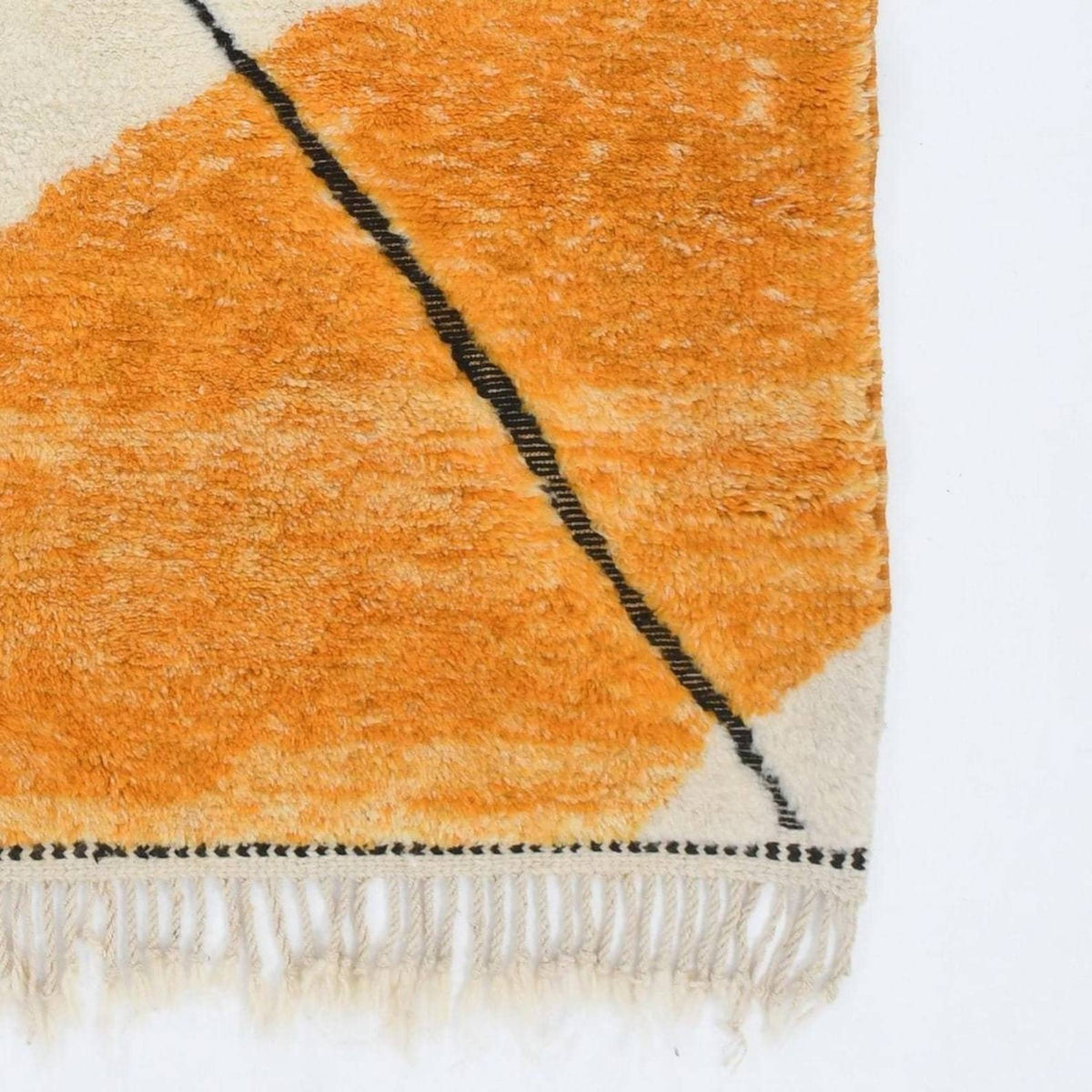 Detail close-up of the orange and cream geometric pattern rug with fringe edges.