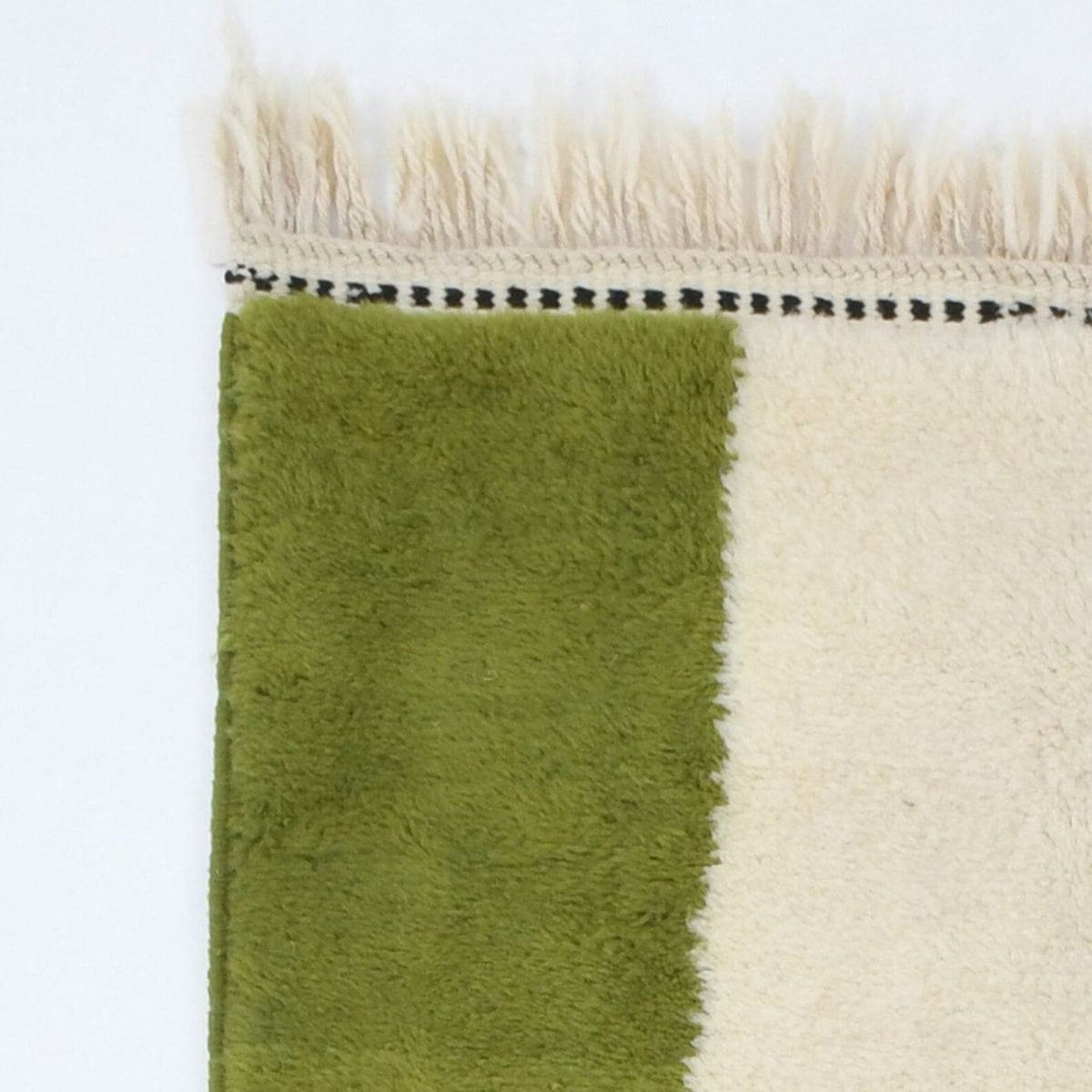 Detail close-up of the solid green and cream rug with fringe edges.