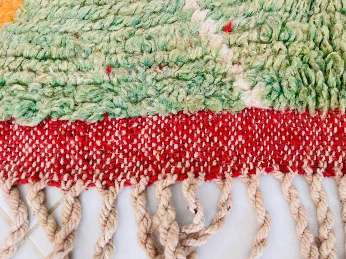 Close-up of the rug's braided edge with colorful strands in green, red, and beige.