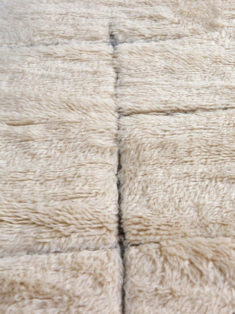 Detail close-up of an off-white textured Beni Ourain Moroccan rug on a white background.