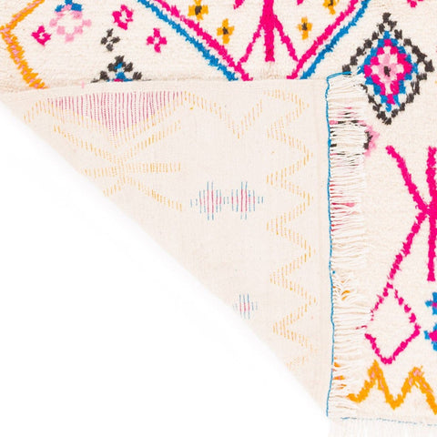 Detail shot of a colorful patterned rug in pink and orange with geometric designs.