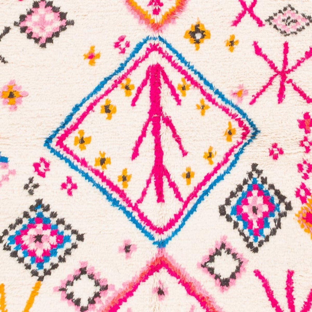 Close-up detail of the corner of a pink and yellow tribal rug with fringe edges.