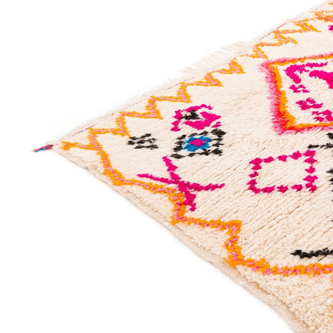 Detail shot of a colorful patterned rug in pink and orange with geometric designs.