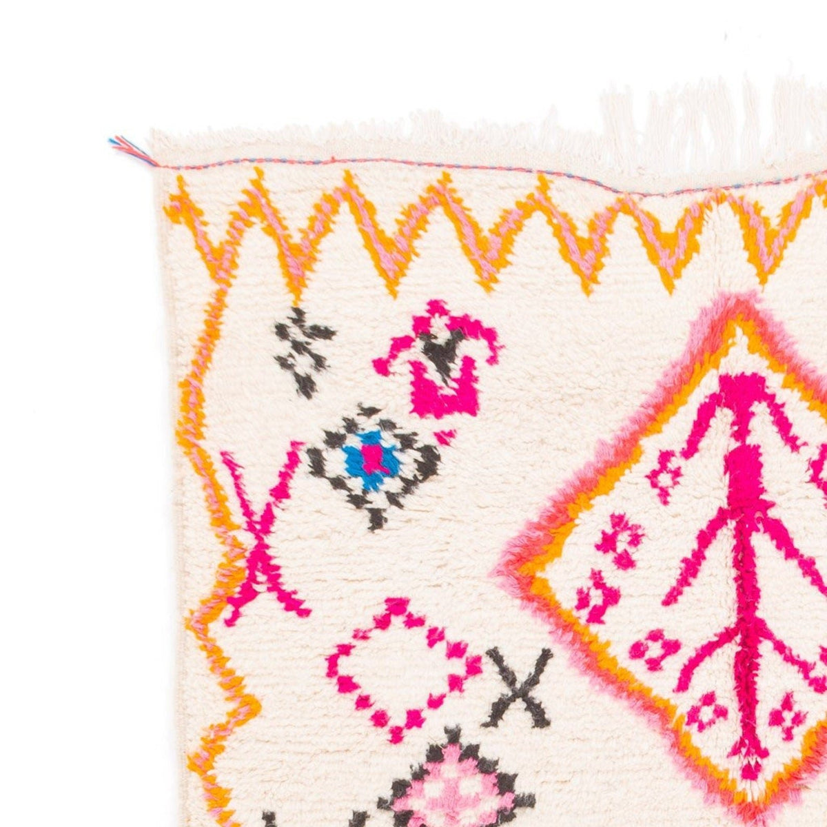 Close-up detail of the edge of a pink and yellow tribal rug featuring geometric patterns.