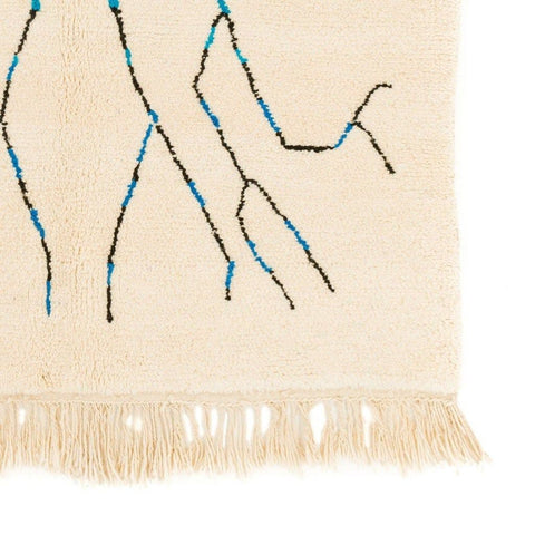 Close-up detail of the fringe on the cream tree design rug with abstract patterns in beige, black, and blue.