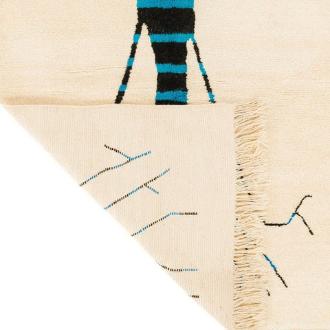 Side view of the cream tree design rug displaying its tree design and fringe edges in cream, blue, and black.