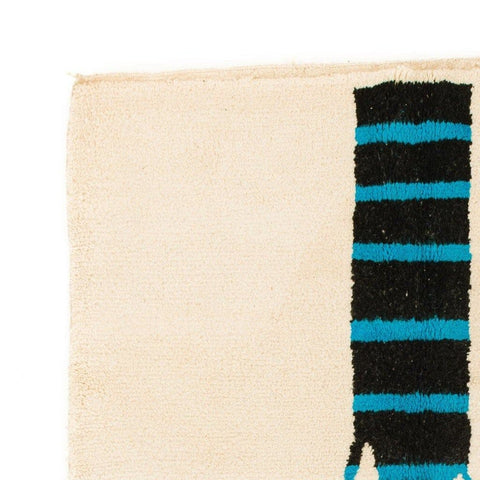 Detail view of the cream tree design rug with fringe edges, featuring a geometric design in cream, black, and blue.