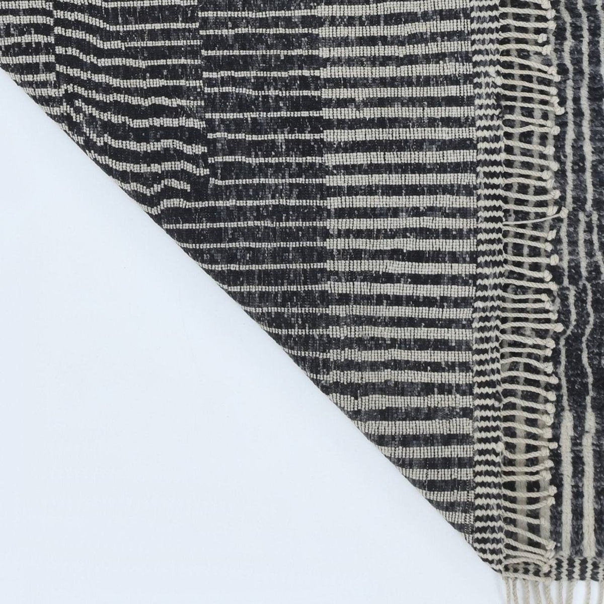Close-up detail of a black and white rug displaying a striped pattern and fringe edges.