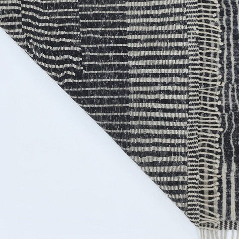 Close-up detail of a black and white rug displaying a striped pattern and fringe edges.