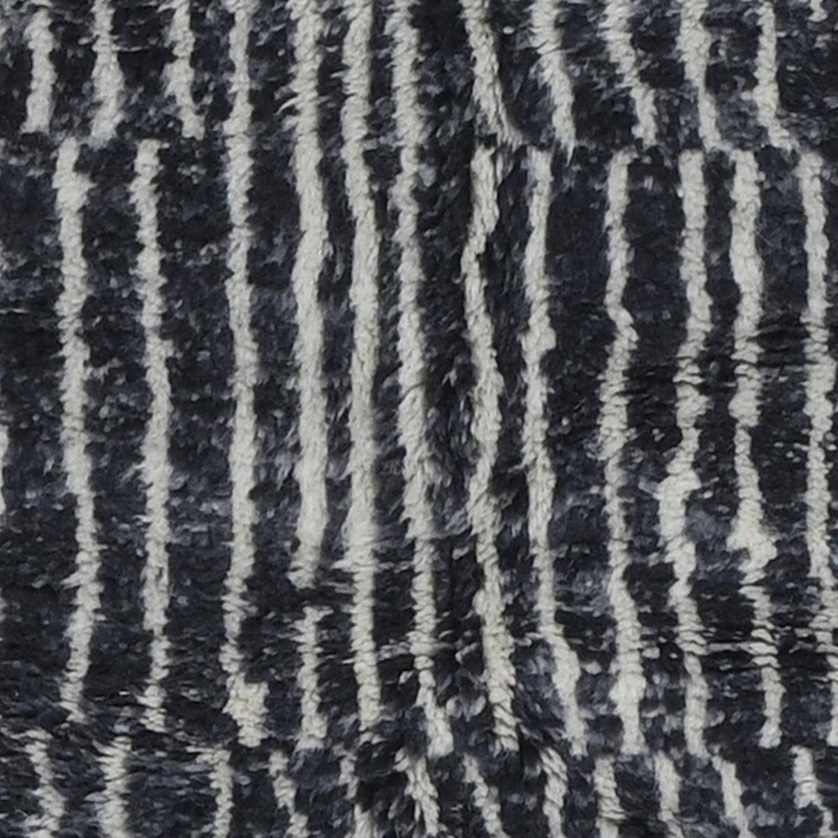 Close-up detail of a black and white rug featuring a striped pattern and fringe edges.