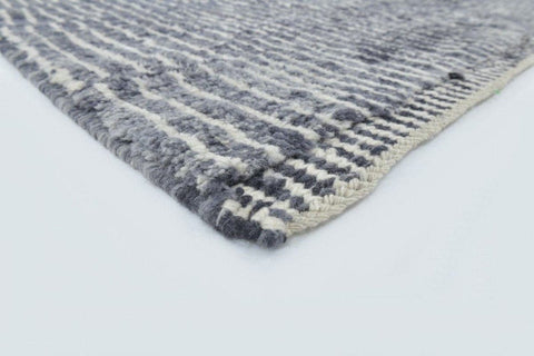Detail shot of the corner of a black tribal rug with fringe edges and a textured surface.